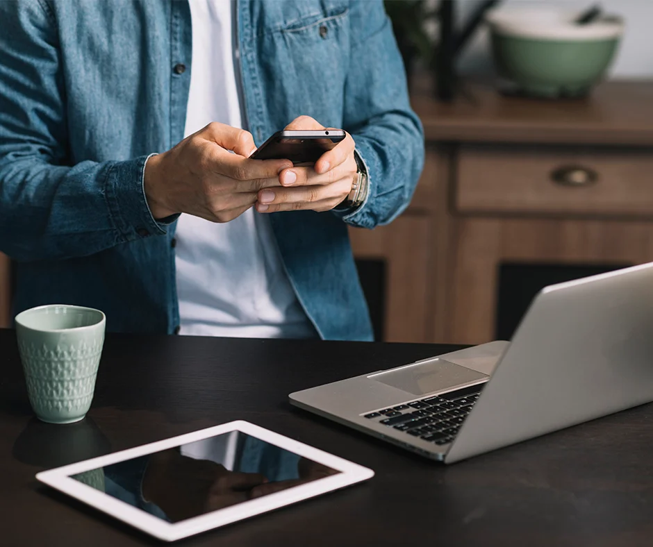 mid-section-young-man-using-smartphone-with-laptop-digital-tablet-coffee-mug-kitchen-counter 940x768